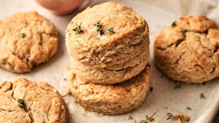 Four golden brown biscuits on parchment paper, with two stacked and garnished with small sprigs of fresh thyme.