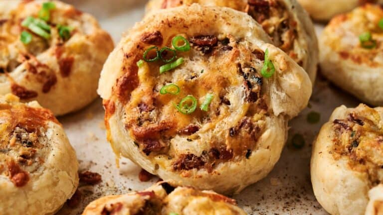 Close-up of savory pinwheel pastries topped with chopped green onions and melted cheese, displayed on a baking tray.