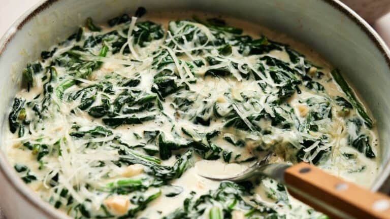 A pan filled with creamy spinach topped with shredded cheese and a spoon partially visible on the right side.