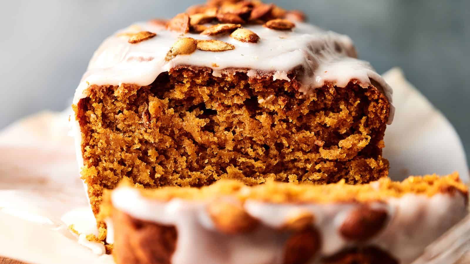 A close-up of a sliced pumpkin loaf cake with white icing and pumpkin seeds on top, showing its moist and crumbly texture.