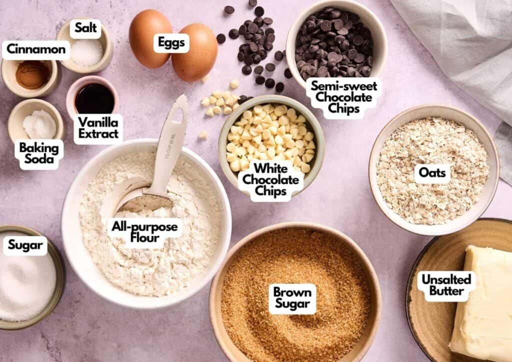 Various baking ingredients for Marry Me Cookies, including flour, oats, eggs, chocolate chips, butter, brown sugar, white sugar, vanilla extract, baking soda, salt, and cinnamon, arranged on a countertop.