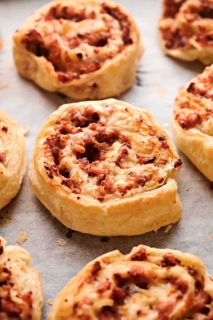 Close-up of several baked Sausage Pinwheels filled with a savory minced meat mixture, arranged on parchment paper.