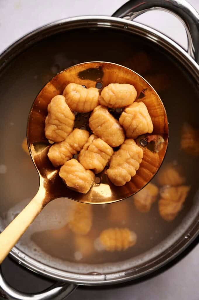 A slotted spoon holds cooked sweet potato gnocchi above a pot of cloudy hot water.