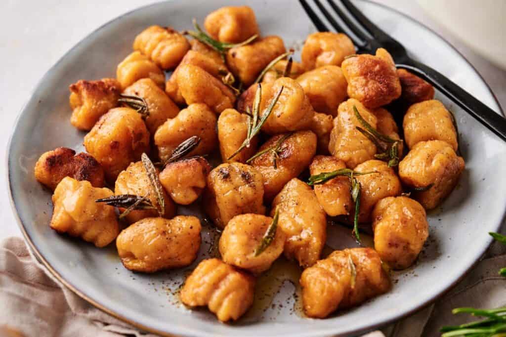 A plate of browned sweet potato gnocchi garnished with herbs, served with a fork on the side.