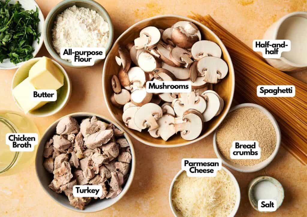 Ingredients for Turkey Tetrazzini are neatly arranged on a countertop, including mushrooms, spaghetti, turkey, broth, cheese, flour, butter, bread crumbs, salt, and half-and-half.