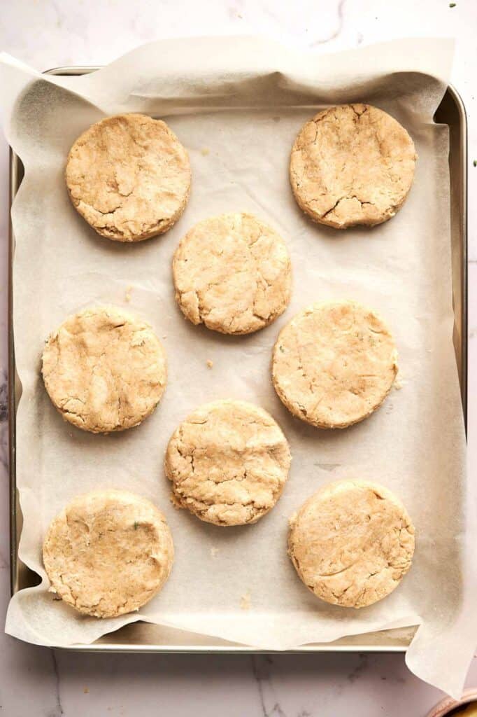 Eight unbaked Cheddar Biscuits arranged on a parchment-lined baking sheet.