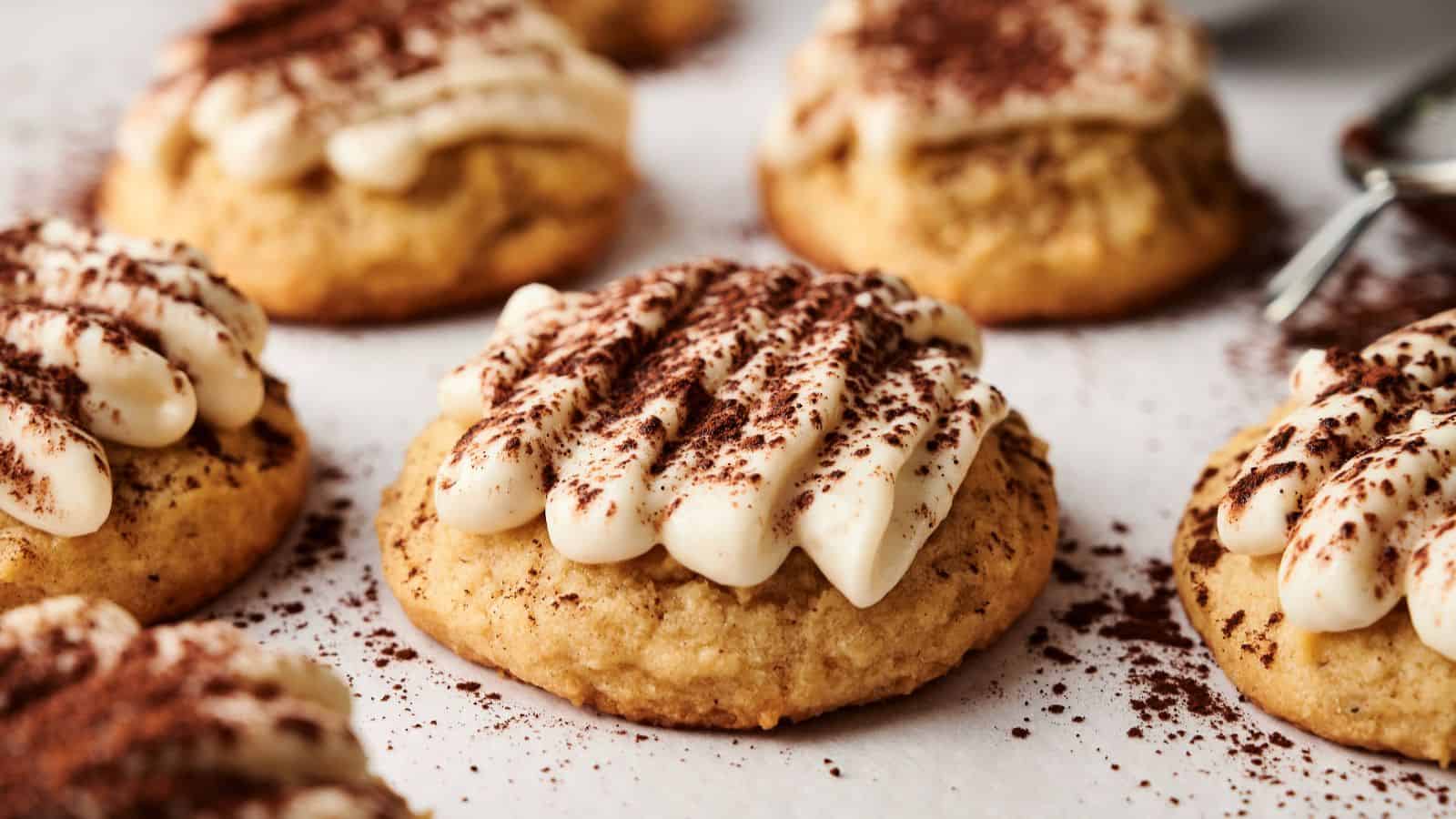 Close-up of cookies topped with piped cream and dusted with cocoa powder, arranged on a white surface.