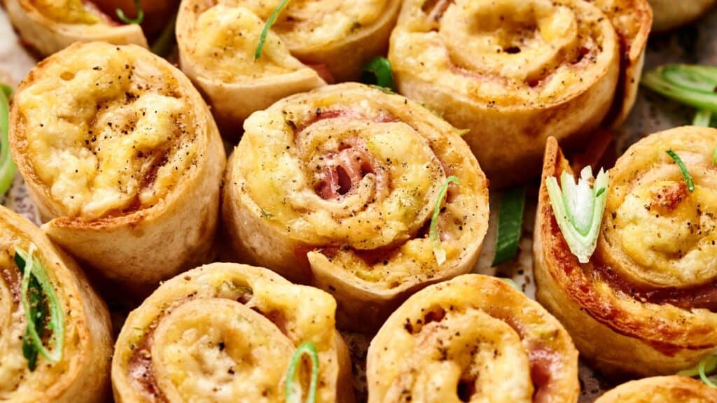 Close-up of baked pinwheel appetizers made with pastry, cheese, and herbs, garnished with sliced green onions.