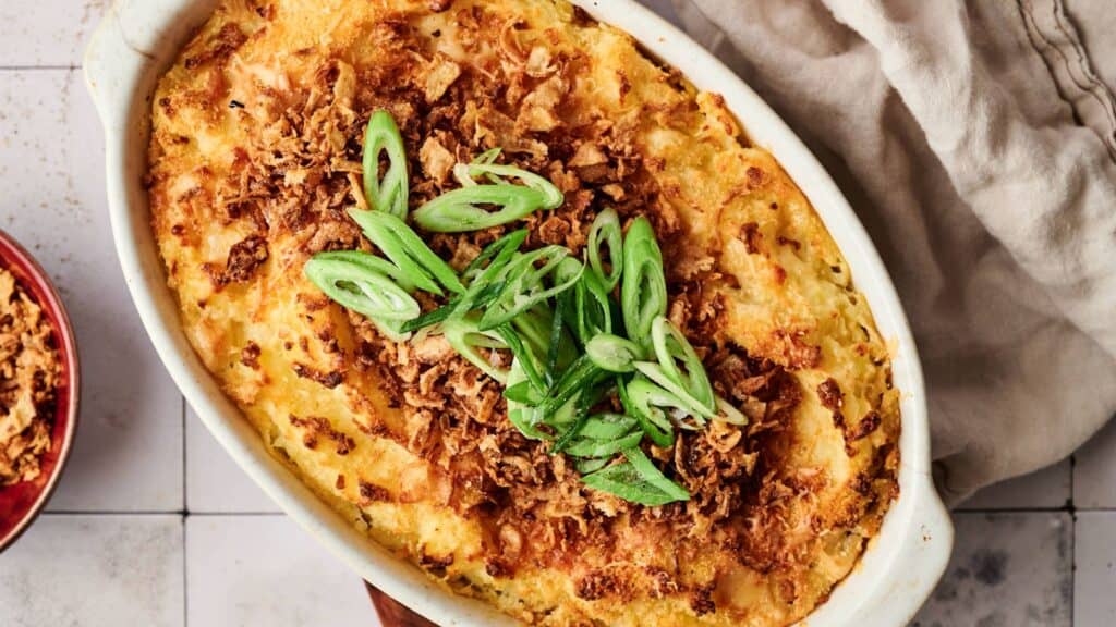 A baked casserole topped with crispy fried onions and sliced green onions, served in an oval dish on a light-colored tiled surface.