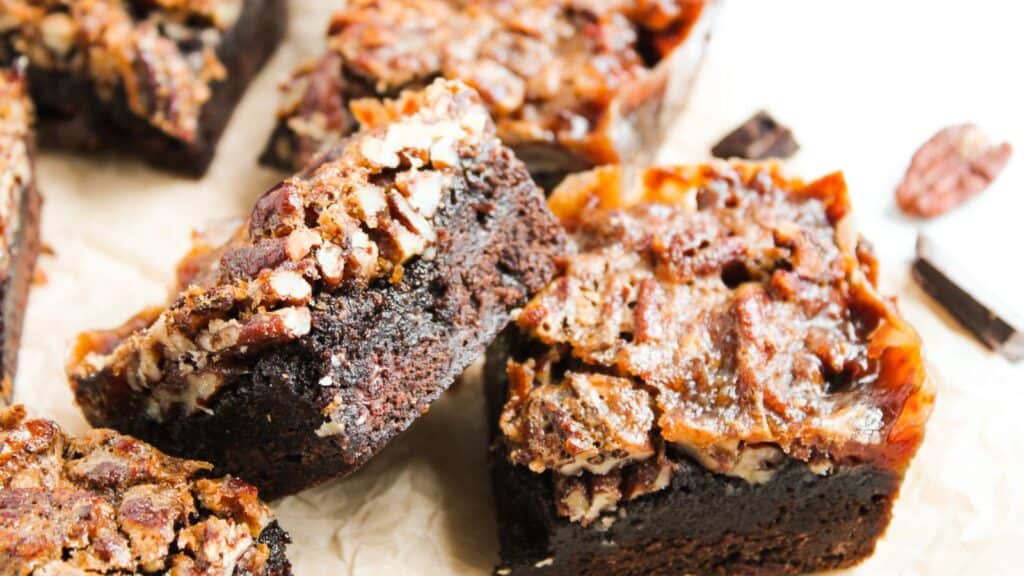 Close-up of several pecan-topped chocolate brownies on a piece of parchment paper.
