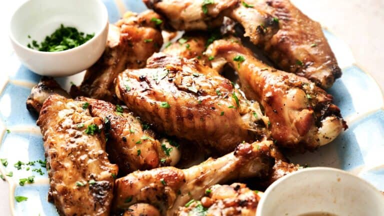 A plate of seasoned, cooked chicken wings garnished with chopped herbs, with two small bowls containing sauce and herbs on the side.