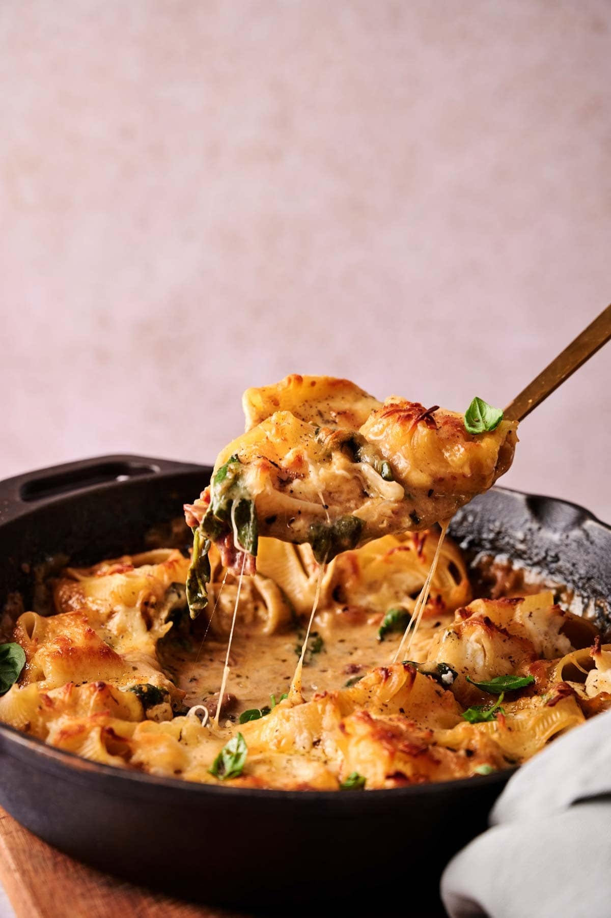 A close-up of Marry Me Chicken Stuffed Shells in a skillet, with a serving being lifted out, reveals gooey melted cheese and savory spinach filling.