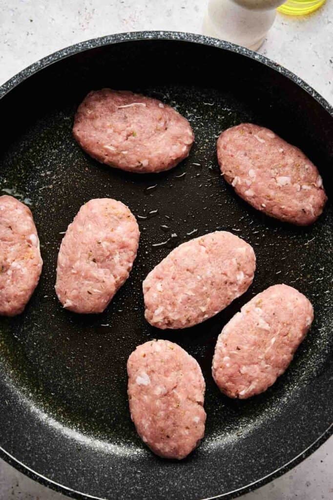 Raw oval-shaped turkey sausage patties arranged in a black skillet, ready to be cooked.