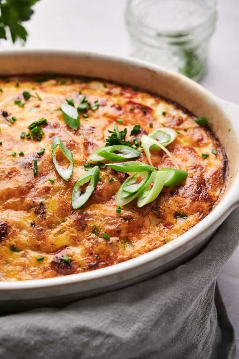 A savory Breakfast Casserole topped with sliced green onions and chopped chives, served in a round ceramic dish.