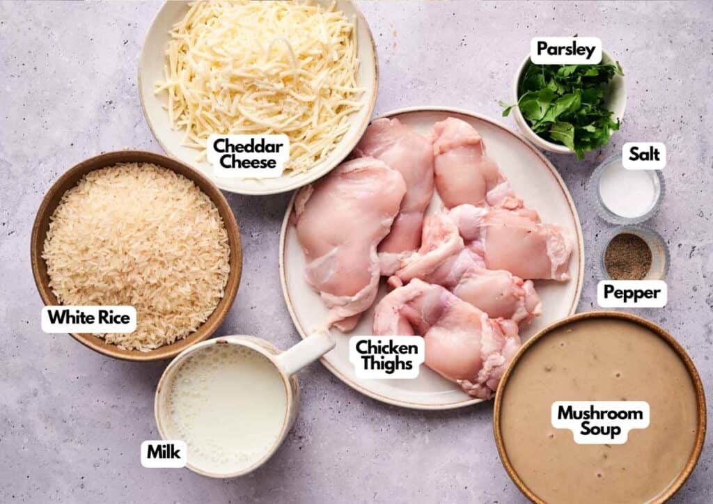A flat lay of raw chicken thighs, shredded cheddar cheese, white rice, milk, mushroom soup, chopped parsley, salt, and pepper in separate bowls—perfect for preparing a classic Chicken and Rice Casserole.