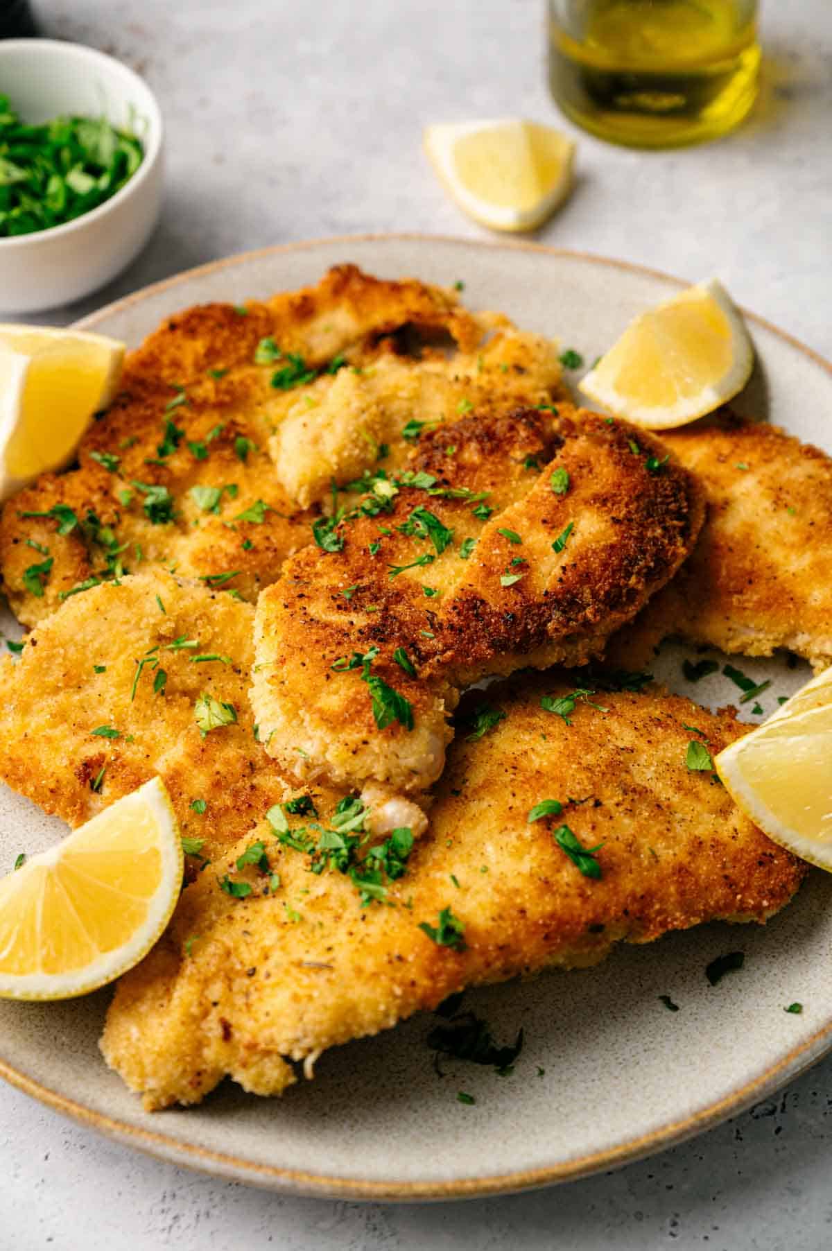 A plate of crispy chicken cutlets, breaded and fried to perfection, garnished with chopped herbs and served with fresh lemon wedges.