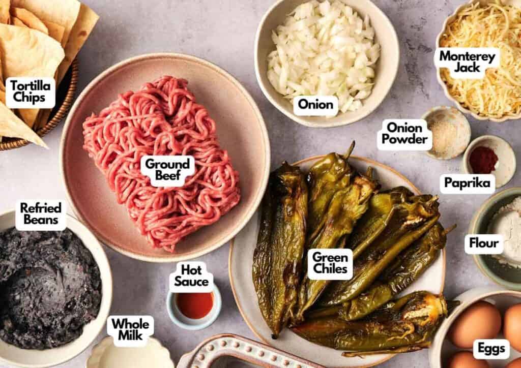 A top-down view of labeled ingredients for Air Fryer Chili Relleno Casserole, including ground beef, green chiles, onion, Monterey Jack cheese, eggs, flour, and other assorted items.
