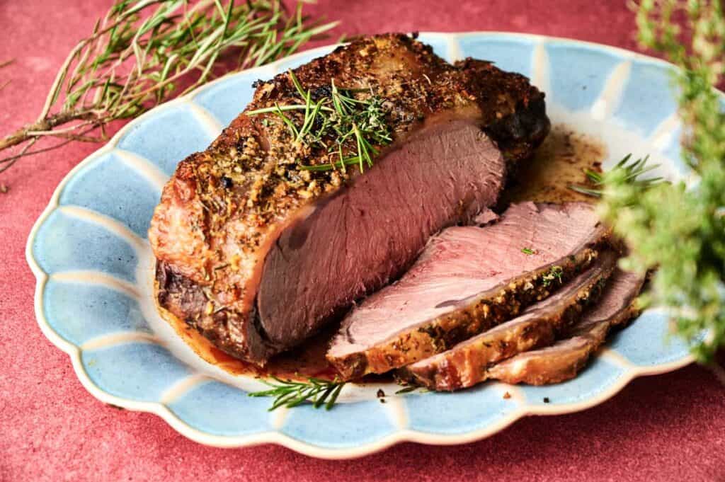 A Christmas Prime Rib Roast with a savory herb crust, partially sliced on a blue scalloped plate and garnished with fresh rosemary.