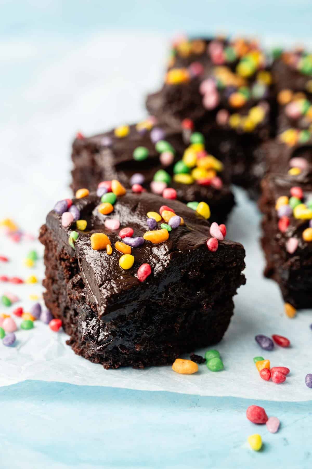 A close-up of Cosmic Brownies topped with colorful candy sprinkles, arranged on a light blue surface.