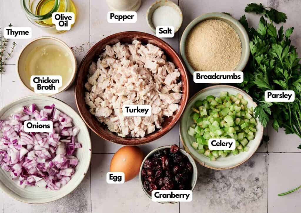 Overhead view of ingredients for Cranberry Turkey Stuffing Balls, including chopped turkey, onions, celery, breadcrumbs, cranberry, egg, chicken broth, olive oil, thyme, salt, pepper, and parsley.
