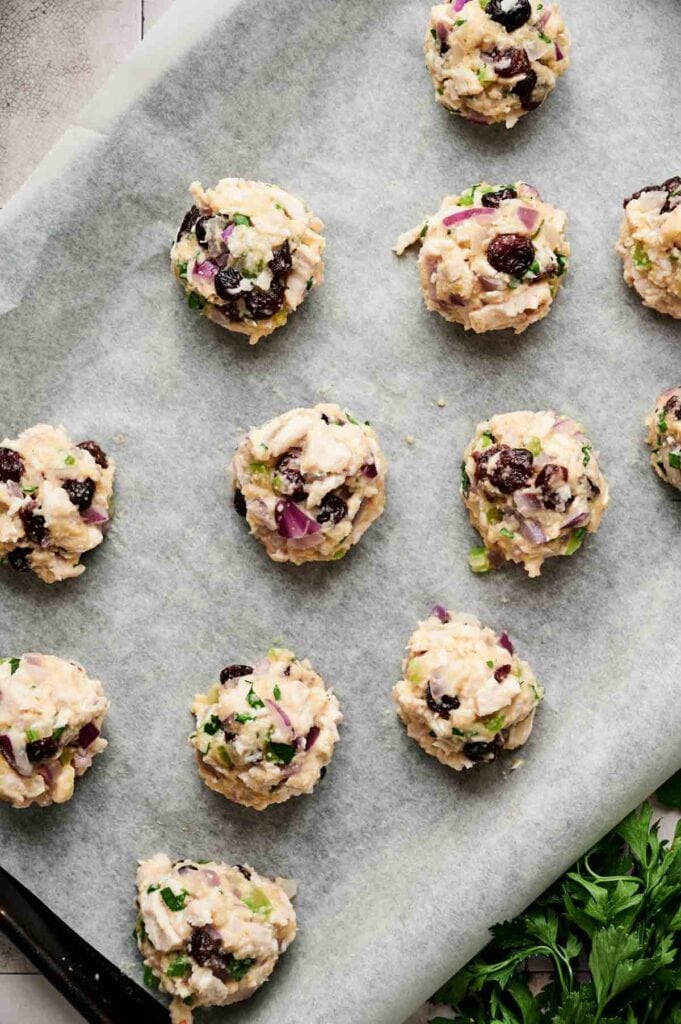 Cranberry Turkey Stuffing Balls&mdash;unbaked chicken salad mixture balls with onions, herbs, and raisins&mdash;are arranged on a parchment-lined baking sheet.