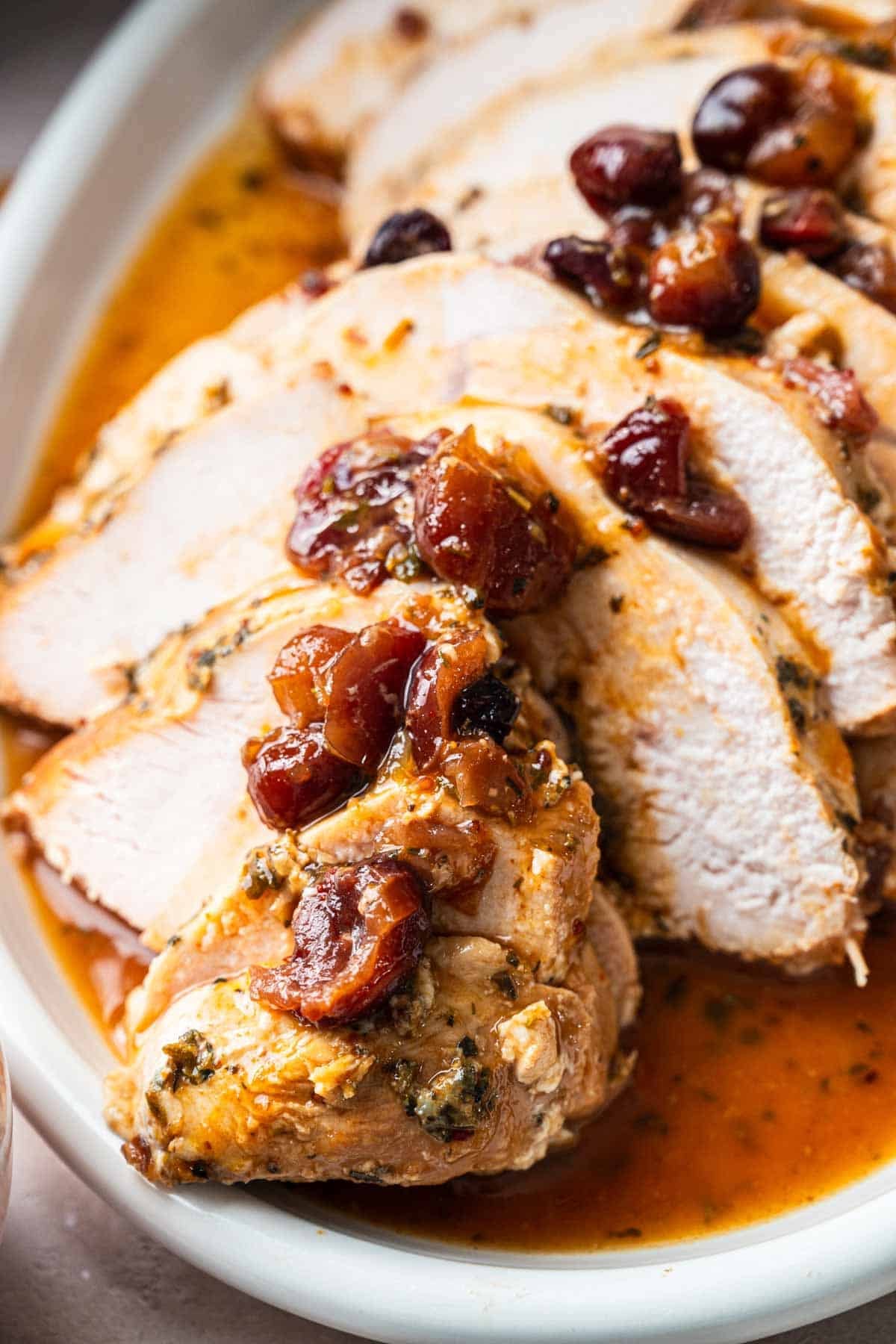 Crockpot Turkey Breast, sliced and topped with a sauce of whole cranberries, served elegantly on a white plate.