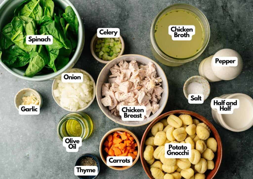 Top-down view of labeled Gnocchi Soup ingredients, featuring chicken breast, potato gnocchi, spinach, celery, onion, garlic, carrots, broth, half and half, olive oil, and seasonings.