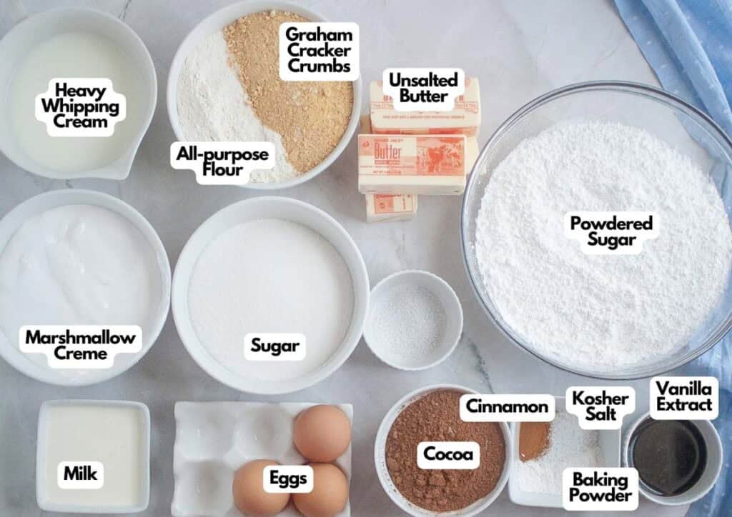 Assorted baking ingredients labeled in bowls and containers, including eggs, flour, sugar, milk, cocoa, powdered sugar, butter, cream, graham cracker crumbs&mdash;perfect for making a delicious Graham Cracker Cake&mdash;and various flavorings.