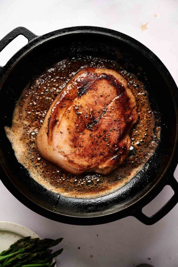 A seared pork chop cooks in a cast iron skillet with bubbling butter and seasoning, delivering the same rich flavors found in classic Ham Steaks.