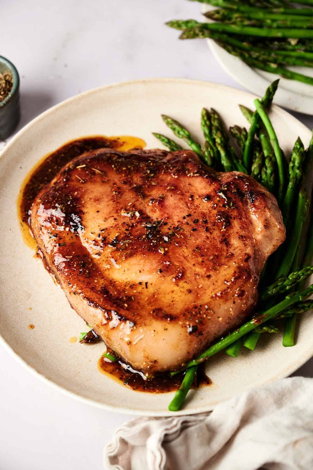 A cooked pork chop with a brown glaze is served on a plate with steamed asparagus spears, reminiscent of classic Ham Steaks dinners.