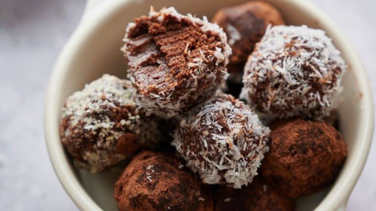 A bowl filled with chocolate truffles coated in shredded coconut and cocoa powder, with one truffle showing a bite taken out of it.