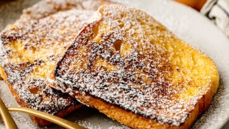 Two slices of French toast dusted with powdered sugar are served on a plate with a fork and knife.