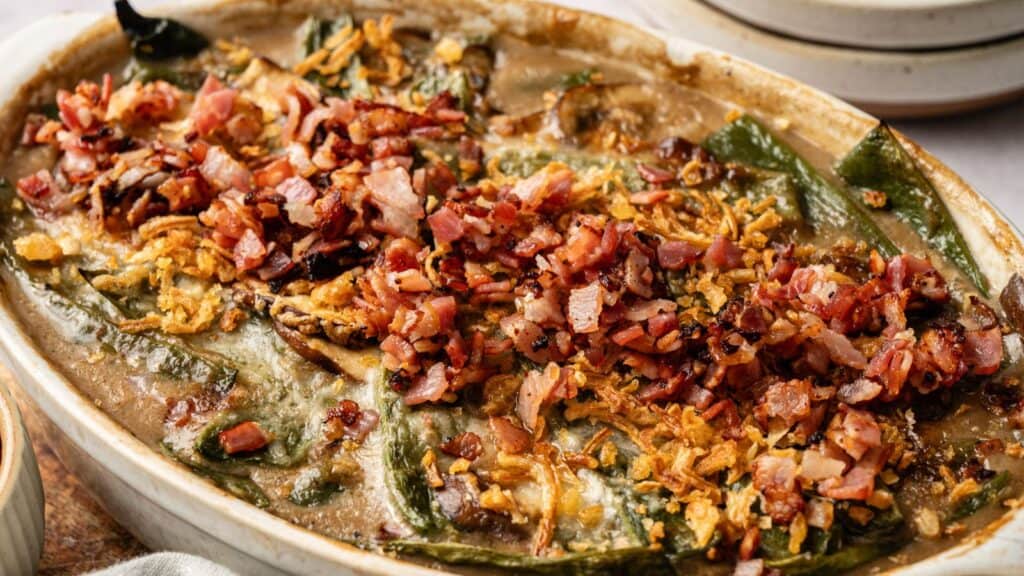 A casserole dish filled with stuffed poblano peppers, topped with crispy bacon bits and fried onions in a creamy sauce.