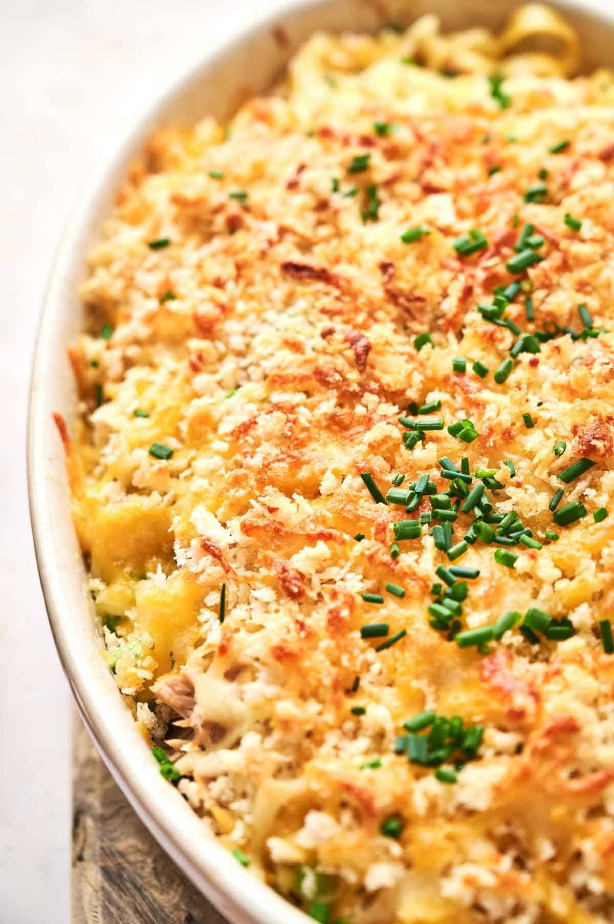 A close-up of a Tuna Casserole topped with golden breadcrumbs and chopped chives in a white oval dish.
