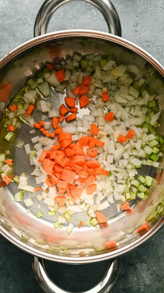 Chopped carrots, celery, and onions are sautéing in a stainless steel pan as the flavorful base for a comforting Gnocchi Soup.