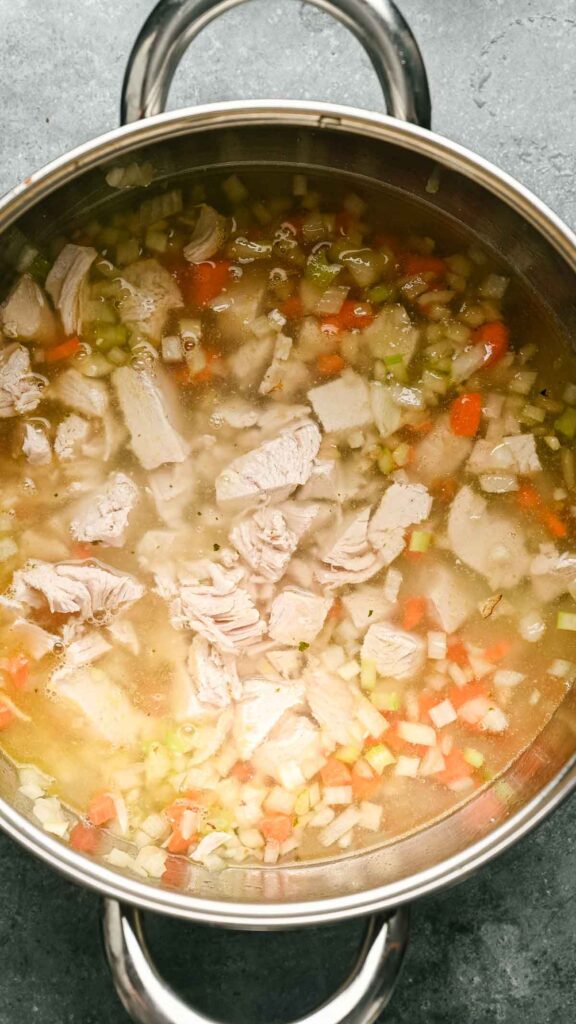 A pot of Gnocchi Soup with chunks of chicken, diced carrots, celery, and onions simmering in broth sits on a gray countertop.
