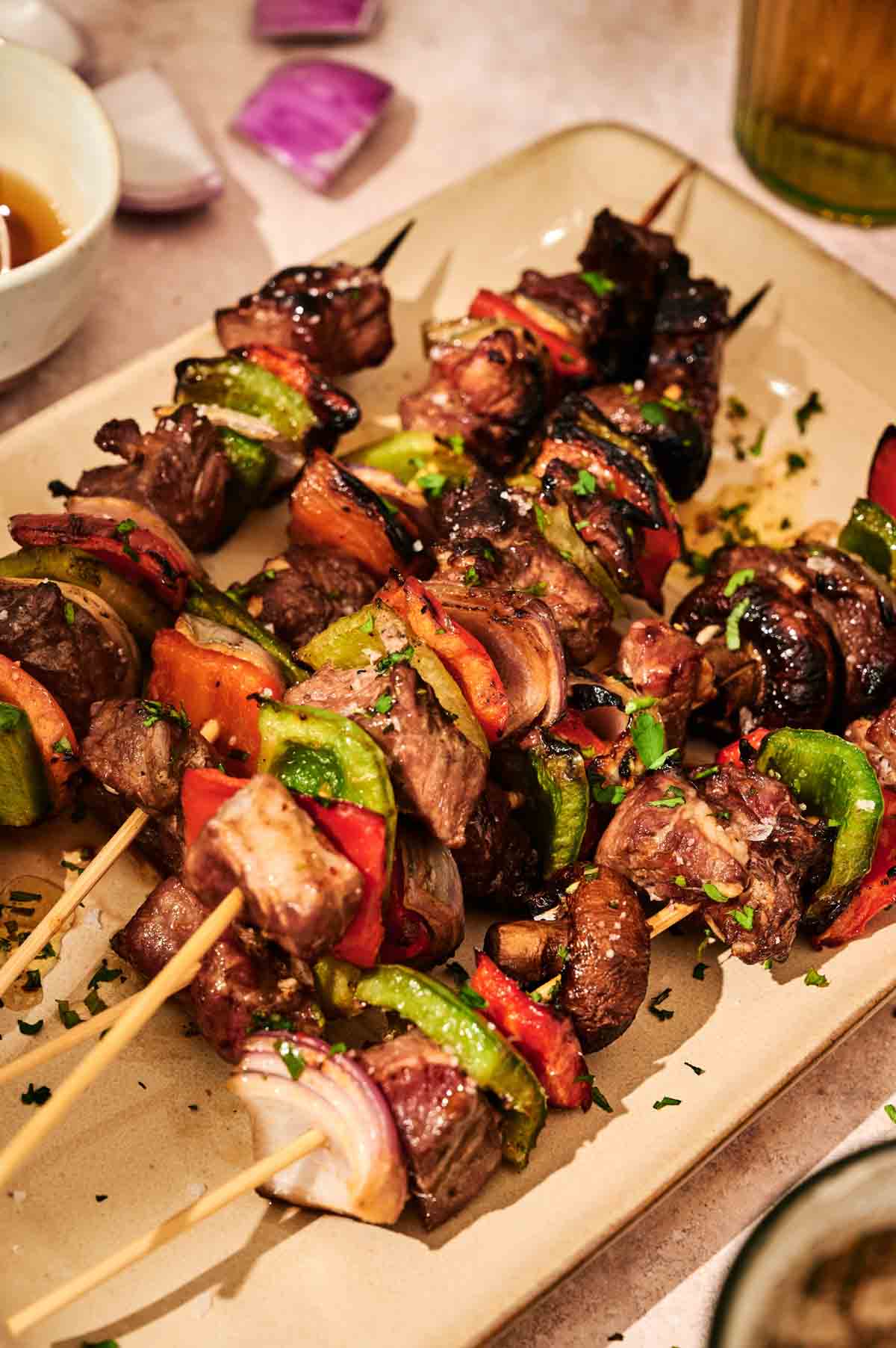 Grilled Beef Kabobs with Chimichurri Sauce, featuring tender beef and vegetable skewers with bell peppers, onions, and mushrooms, served on a beige plate.