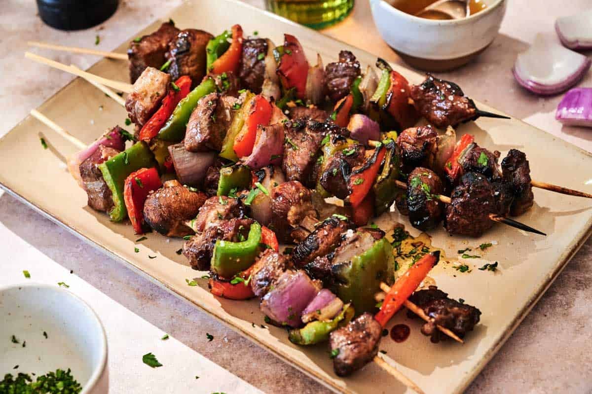 A rectangular plate with Beef Kabobs with Chimichurri Sauce&mdash;grilled beef and vegetable skewers featuring bell peppers, onions, and mushrooms&mdash;garnished with chopped herbs.