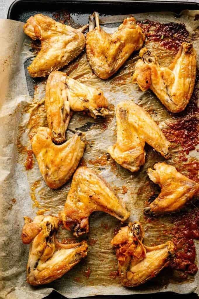 Lemon Pepper Wings baked to perfection are arranged on a parchment-lined baking sheet, boasting a golden-brown color with caramelized spots.