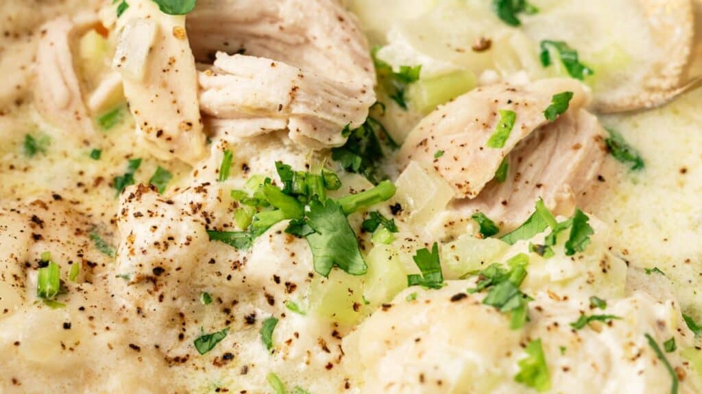 Close-up of creamy chicken and dumplings garnished with chopped parsley and freshly ground black pepper.