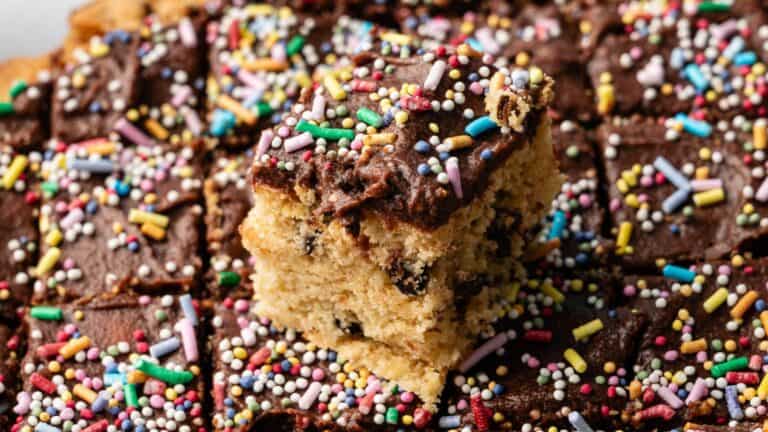 A close-up of chocolate-frosted blondie bars topped with colorful sprinkles, with one bar placed on top of the others.