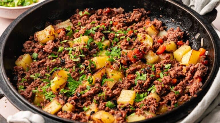 A skillet filled with a ground beef and diced potato hash, garnished with chopped parsley.