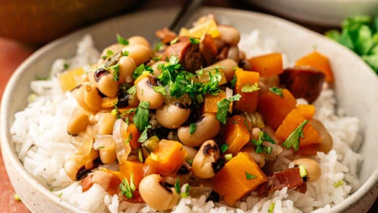 A bowl of white rice topped with a mixture of black-eyed peas, diced carrots, onions, and herbs.