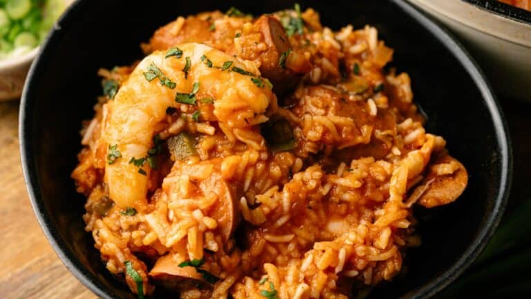 A bowl of jambalaya with shrimp, rice, sausage, and vegetables, garnished with chopped herbs.
