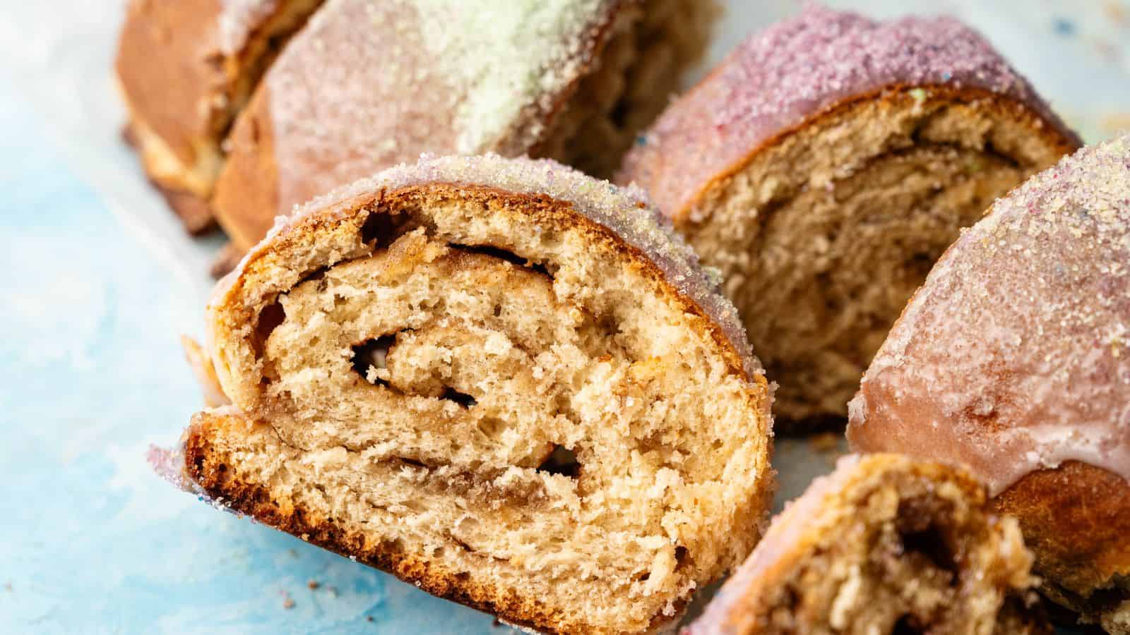 Close-up of sliced sweet bread with a swirled filling and colorful sugar topping on a light blue surface.