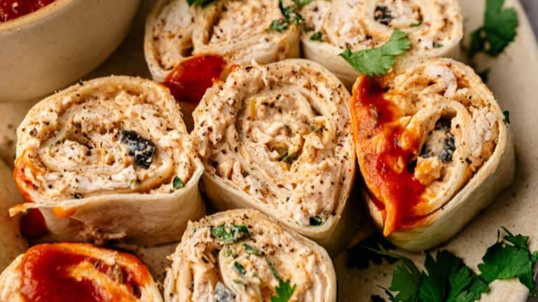 Close-up of tortilla pinwheels filled with seasoned chicken and herbs, garnished with cilantro and topped with a red sauce.