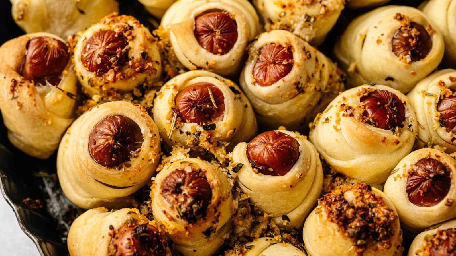 Close-up of baked pigs in a blanket, small sausages wrapped in golden-brown dough and sprinkled with seasoning.