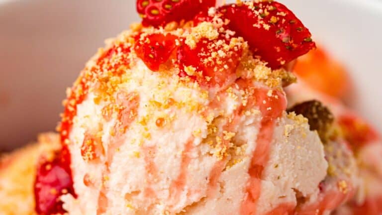 Close-up of a scoop of ice cream topped with strawberry pieces, strawberry sauce, and a sprinkle of crushed cookie crumbs.