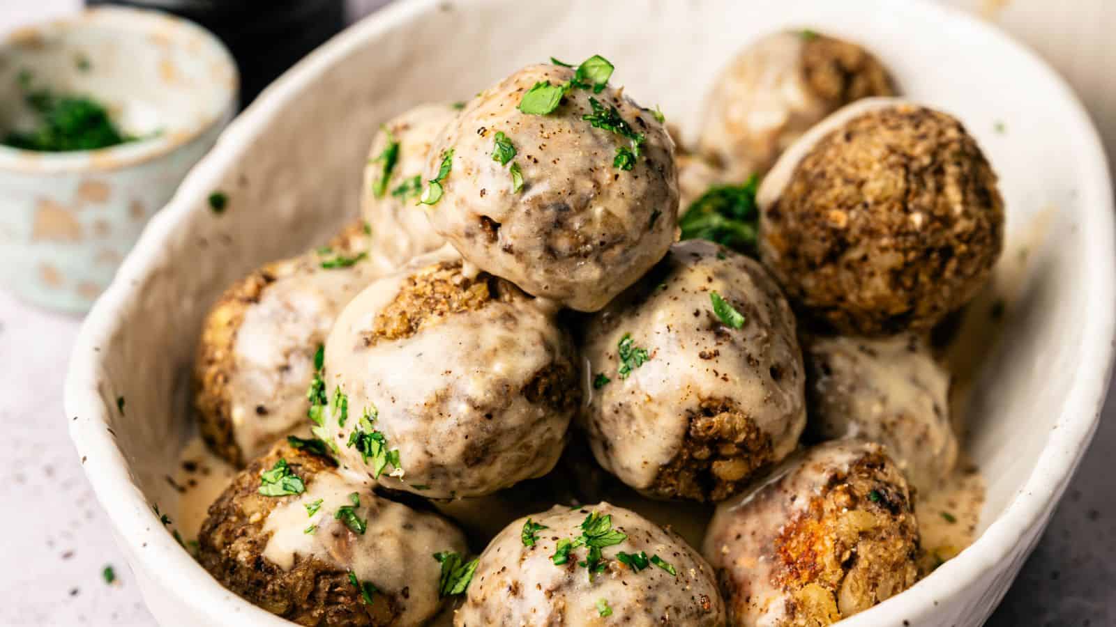 A white bowl filled with meatballs topped with creamy sauce and garnished with chopped fresh herbs.