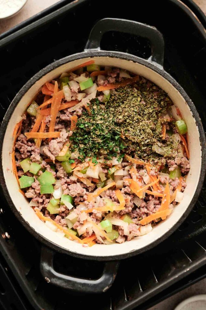 A pot filled with cooked ground meat, chopped carrots, celery, onions, and a pile of dried herbs comes together to create the perfect base for Air Fryer Cheeseburger Soup.